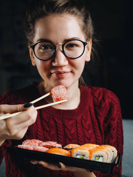 Woman with chopsticks and sushi rolls in plastic container. - Fotó, kép