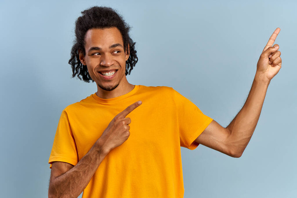 Active smiling african american young guy in yellow shirt points finger - Photo, image