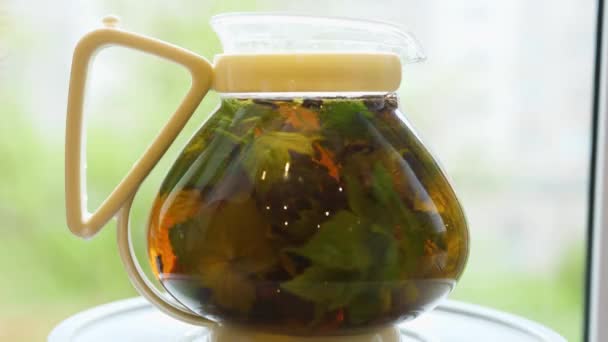 スグリ、レモンバーム、ミント、ラズベリーの葉をグラスティーポットでお茶を醸造します。ティーパーティー屋外 - 映像、動画