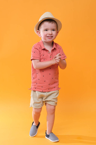 Bardzo szczęśliwy chłopiec w letnim stroju. Studio strzelać na pomarańczowym tle. - Zdjęcie, obraz