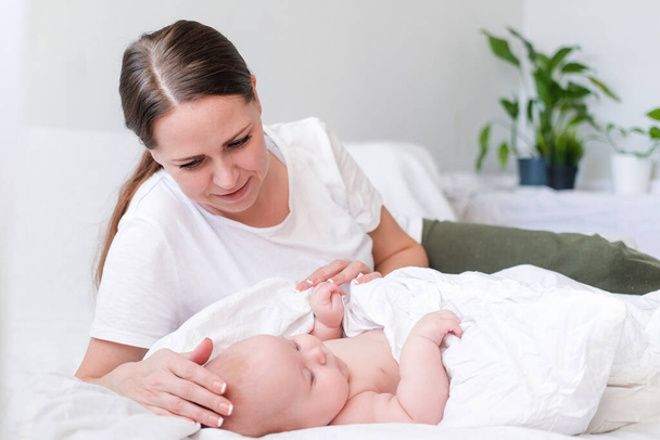 Mother love. Caucasian young brunette woman mom looking to her little cutest baby lying in bed. Infant child. Family life. Mother and baby. Happy motherhood - Zdjęcie, obraz