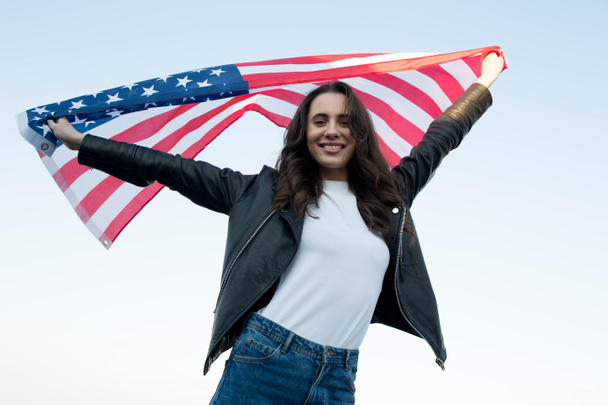Mladá žena mává americkou vlajkou proti modré obloze - Fotografie, Obrázek