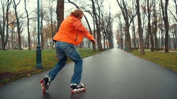 Experienced bearded male skater technically and virusically performs complex U-turns and tricks on the asphalt road of a park alley among trees and grass in the spring. Weekend active leisure concept. - Footage, Video