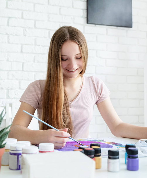 улыбающаяся молодая художница рисует на одежде в своей студии
 - Фото, изображение