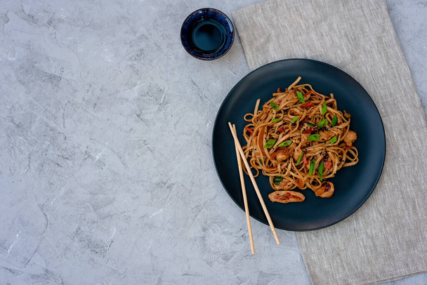 Asian udon noodles with chicken vegetables and teriyaki sauce with chopsticks and a linen napkin on a gray concrete background. Chinese and Japanese cuisine. Copy space. - Photo, Image