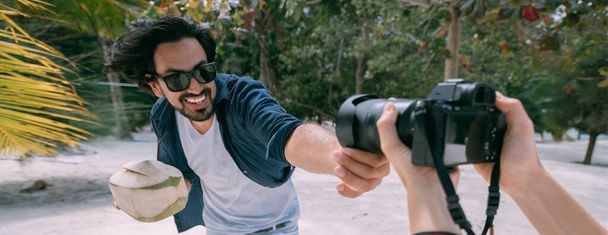 Счастливый парень и фотограф на тропическом пляже. Фотосессия с профессиональным фотографом на фоне пальм с кокосом в руках
. - Фото, изображение
