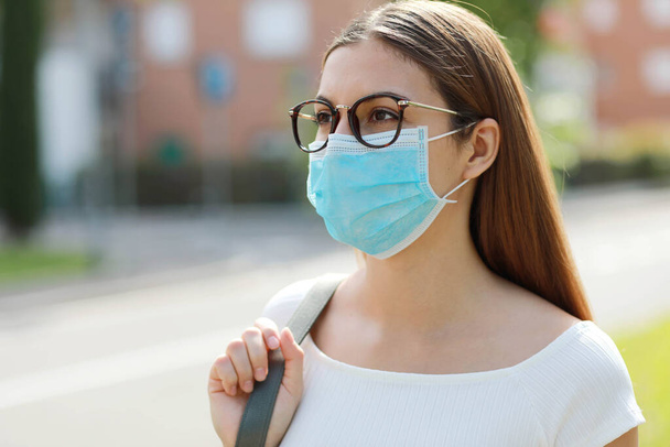 Nuori nainen kaupungin kadulla yllään suojaava naamio leviämisen taudin virus SARS-CoV-2. Tyttö, jolla on kirurginen naamio kasvoilla sepelvaltimotautia vastaan 2019. - Valokuva, kuva