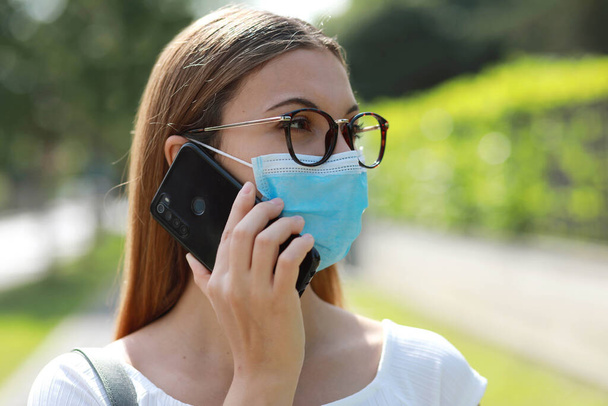 Тщательная деловая женщина разговаривает по смартфону в хирургической маске, избегая коронавируса на городской улице
 - Фото, изображение