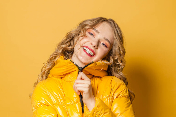 Happy young woman in yellow winter jacket on bright yellow background, close up portrait - Foto, imagen