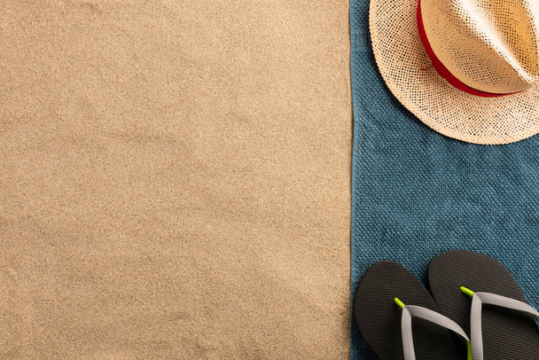 Hat and flip flops on the towel with sand background. Harsh light with shadows.  - Fotografie, Obrázek