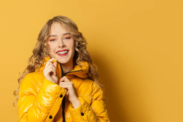 Joven mujer sonriente en chaqueta de invierno sobre fondo amarillo brillante, primer plano retrato
 - Foto, Imagen