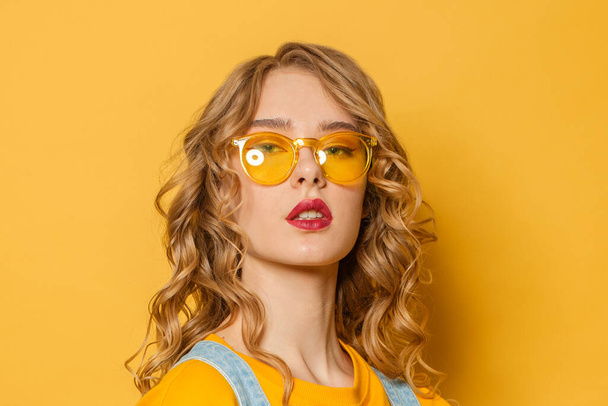 Mujer modelo de moda con cabello rubio rizado sobre fondo amarillo brillante, primer plano retrato
 - Foto, imagen