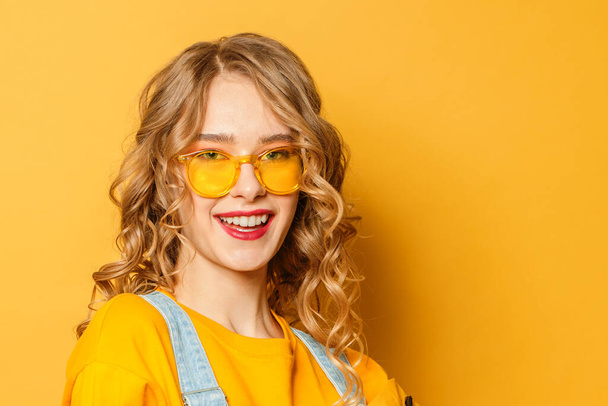 Szczęśliwa uśmiechnięta kobieta w okularach przeciwsłonecznych na żółtym tle - Zdjęcie, obraz