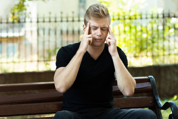 Portrét hezkého muže se stresem a bolestí hlavy s migrénou v parku - Fotografie, Obrázek