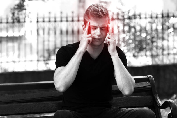 Retrato de un hombre guapo con estrés y dolor de cabeza con migraña en el parque. Blanco y negro con acento rojo
 - Foto, Imagen
