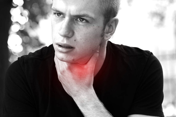 Молодий чоловік з болем у горлі стоїть в парку і рука торкається його Ілл шиї. Чорно-білий з червоним акцентом
 - Фото, зображення