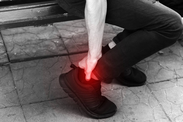 Tobillo torcido. Un joven tocándose la pierna torcida en el parque. Blanco y negro con acento rojo
 - Foto, Imagen