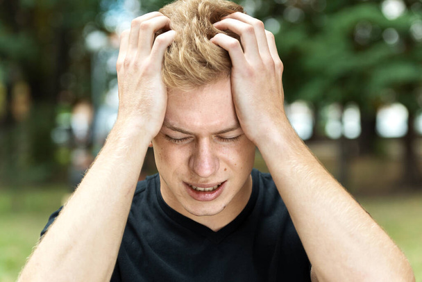 Πορτρέτο ενός όμορφου άντρα με άγχος και πονοκέφαλο που έχει ημικρανία στο πάρκο - Φωτογραφία, εικόνα