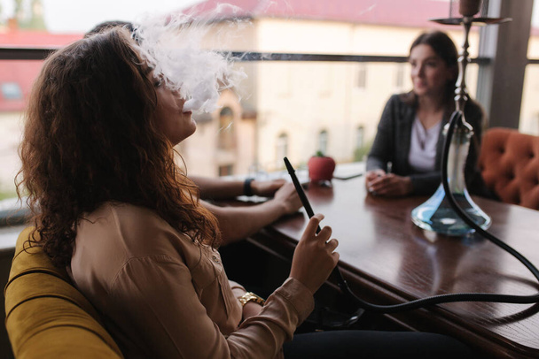 Groep mensen rookt hookah op het terras. Mannen en vrouwen ontmoeten elkaar in restaurant - Foto, afbeelding