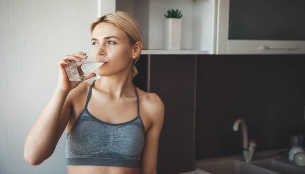 Close up photo of a caucasian woman drinking water after practicing home fitness - Foto, Imagen