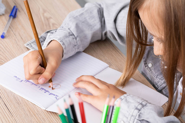 La fille de la leçon s'est vu confier la tâche de dessiner un ours en peluche. La jeune écolière dessine avec des crayons dans un carnet d'école
. - Photo, image