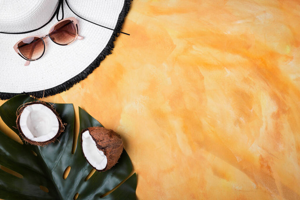 Yaz tatili konsepti düzdü. Palmiye yaprağı ve yaz şapkalı hindistan cevizinin yarısı, sarı süslemeli güneş gözlükleri.. - Fotoğraf, Görsel