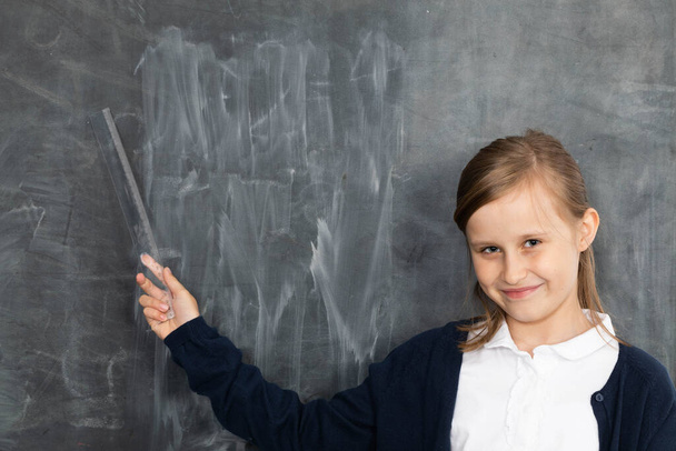 A girl stands smiling at a chalkboard and points to an empty space ready for writing with chalk. - Photo, image