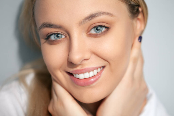 Portrait of a smiling blonde in a white blouse on a light background. - Fotografie, Obrázek