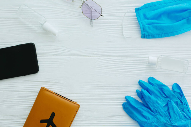 Blue face mask, gloves, antiseptic and disinfectant, passport, sunglasses and phone on white background, copy space. Safe travel in summer 2020.  Coronavirus vacation protection measures - Photo, Image