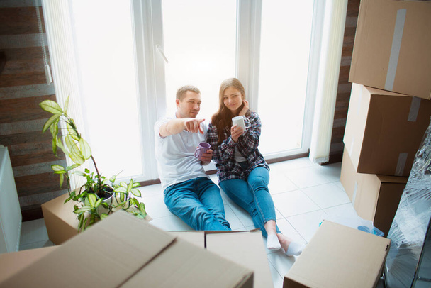 Ein junges Ehepaar sitzt im Wohnzimmer des Hauses am Fenster. Sie freuen sich über ein neues Zuhause. Umzug, Hauskauf, Wohnungskonzept. - Foto, Bild