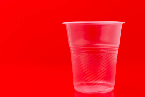 赤い背景に水を飲むためのプラスチック透明使い捨てカップ - 写真・画像