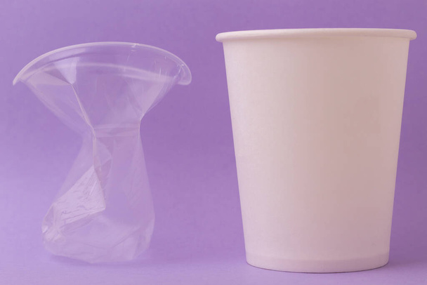 壊れた透明なプラスチックカップと紫の背景に水や熱い飲み物を飲むための環境に優しい紙使い捨てカップ。コンセプトはプラスチックではなく! - 写真・画像