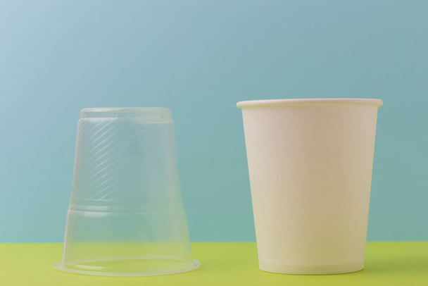Inverted plastic cup and an environmentally friendly paper disposable cup for drinking water and hot drinks on a colored background. Concept no more plastic! - Photo, image