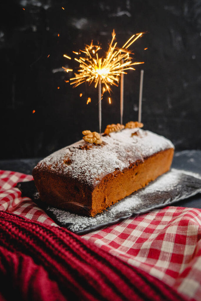 new year pound cake with Christmas spices and a bengal light sparkler. festive traditional bread on a black background with red tablecloth. holiday food. copy paste - Fotografie, Obrázek