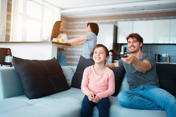 Una gran familia en casa. Mamá y su hija se comunican entre sí. Padre o hermano ver la televisión
. - Foto, Imagen