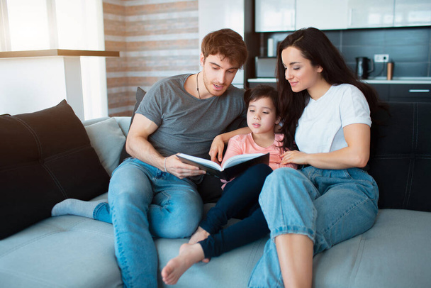 Family at home reading a book. Adult brother and sister reading a book to little sister. Young parents and daughter - Foto, imagen