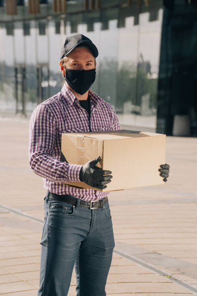 Young man in a medical mask and gloves holds a paper box with documents, vertical photo of the dismissal during a coronavirus pandemic - Fotografie, Obrázek