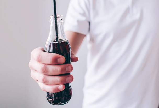 Young man isolated over background. Cut view of males hand holding bottle with coke inside it and plastic black straw. Sweet tasty sugary drink. - Zdjęcie, obraz