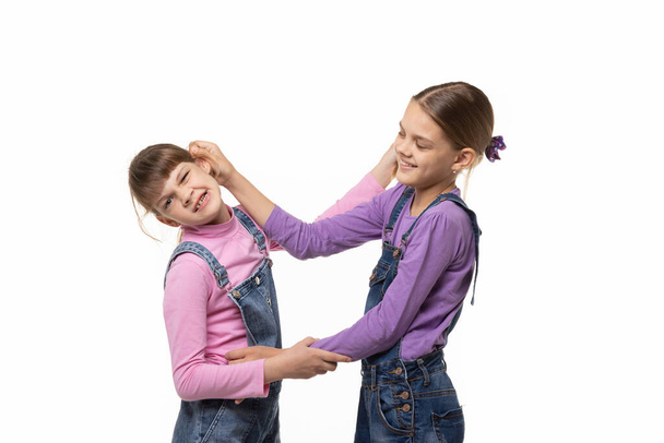 The eldest girl drags the younger one by the ear, isolated - Photo, Image