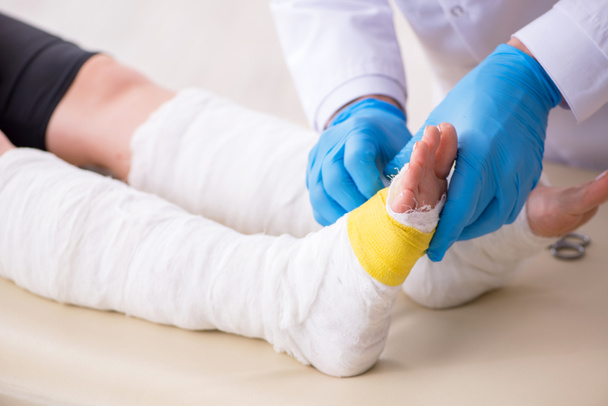 Jonge been gewonde vrouw op bezoek bij oude arts traumatoloog - Foto, afbeelding