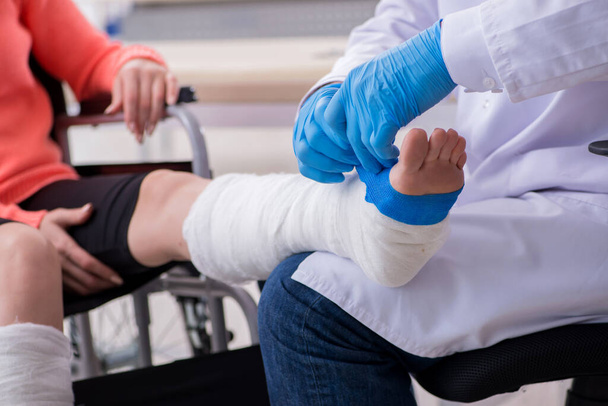 Jeune femme blessée à la jambe rendant visite à un vieux médecin traumatologue - Photo, image