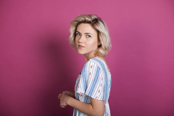 Blonde caucasian woman wearing a modern shirt is looking back to camera on a violet studio wall - Photo, Image