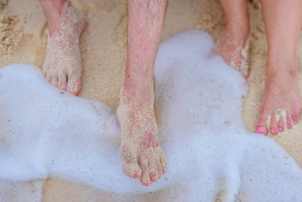 Zwei Beinpaare auf weißem Sand mit Welle - Foto, Bild