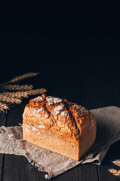 Loaf ruskeaa leipää tekstiili pyyhe tumma puinen pöytä mustalla pohjalla kopioi tilaa - Valokuva, kuva