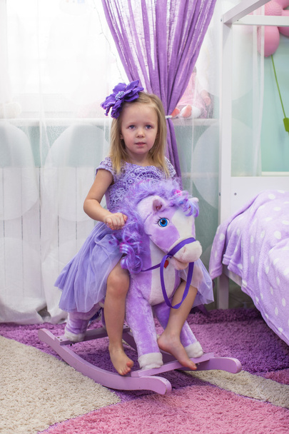 Charming little girl in a dress on horseback riding toy horse - Foto, afbeelding