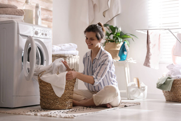 Young woman taking laundry out of washing machine at home - Foto, afbeelding