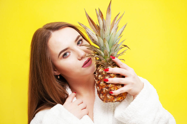 Jonge vrouw met een rijpe ananas in de buurt van haar gezicht - Foto, afbeelding