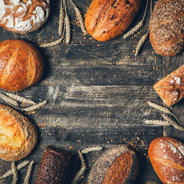 Bread border on wood background with copy space. Square composition of whole grain loaves with spikelets. Different types of bread arranged as frame. Bakery, cooking and grocery store concept. - Fotó, kép