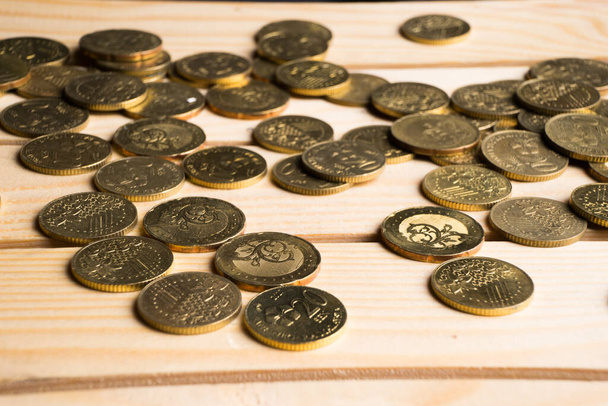 Goldmünzen verstreut auf einer warmen goldfarbenen Holzoberfläche. Finanzen, Buchhaltung, Geldsparen und Anlagekonzept. - Foto, Bild