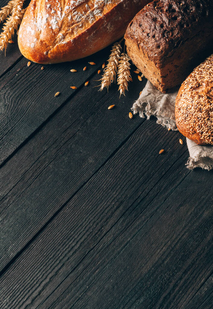 Bread border on black wood background with copy space. Different types of bread arranged as a frame with spikelets in corner. Bakery, cooking and grocery store concept. - Фото, зображення